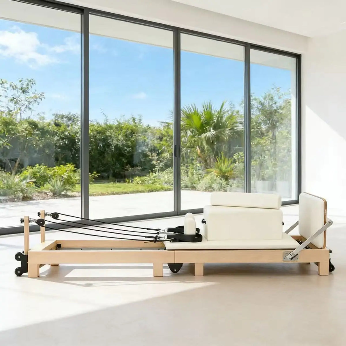 Reformer Pilates en érable, sellerie crème, devant une baie vitrée